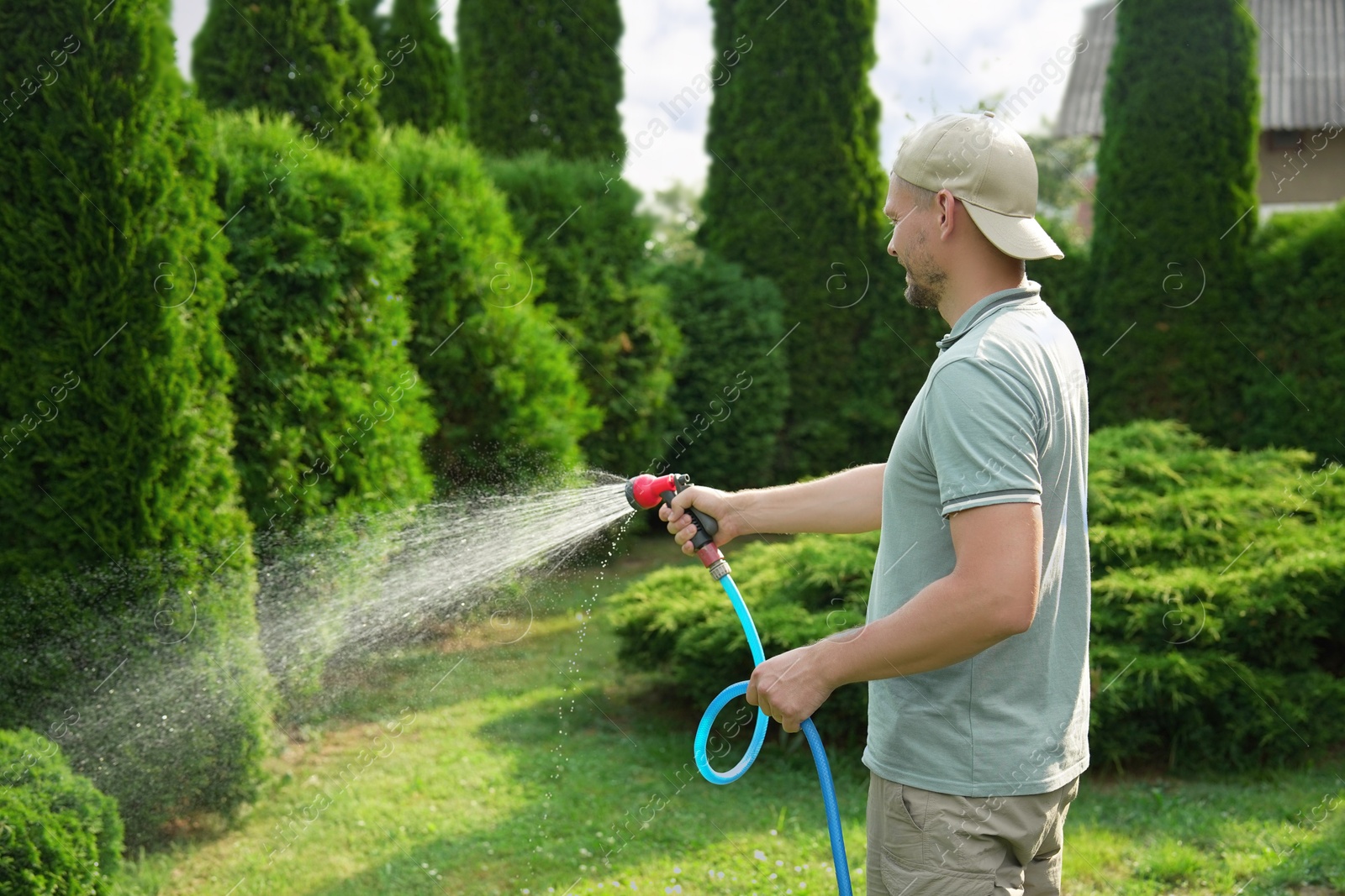 Photo of Man watering lawn with hose in backyard