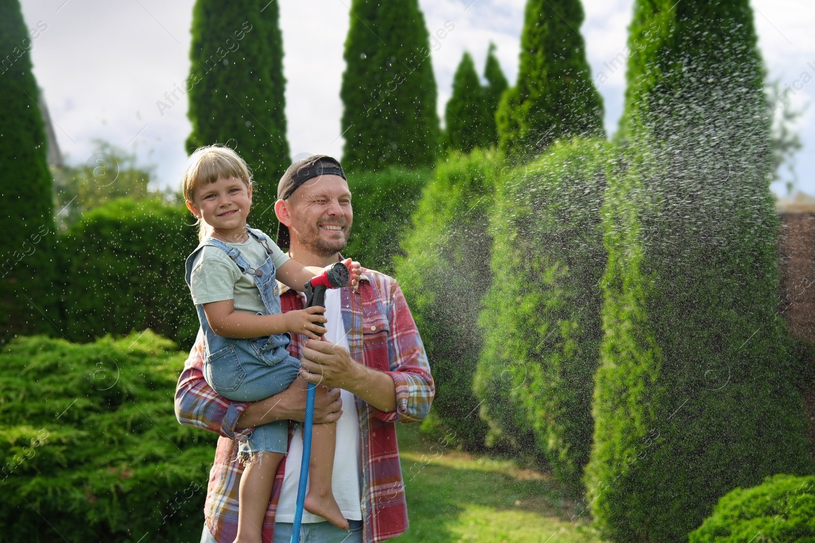 Photo of Father and his daughter watering lawn with hose in backyard