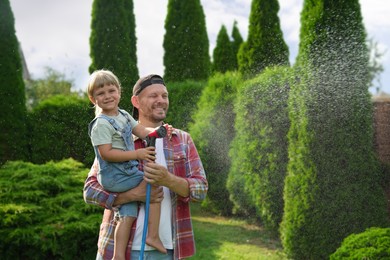 Father and his daughter watering lawn with hose in backyard