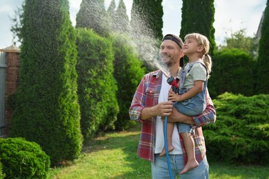 Father and his daughter watering lawn with hose in backyard