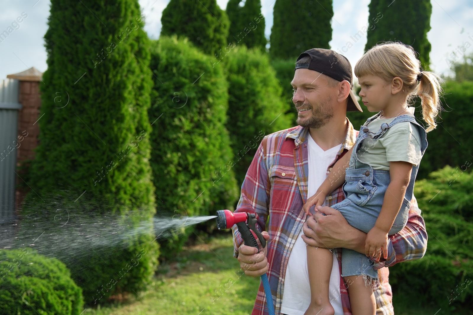 Photo of Father and his daughter watering lawn with hose in backyard