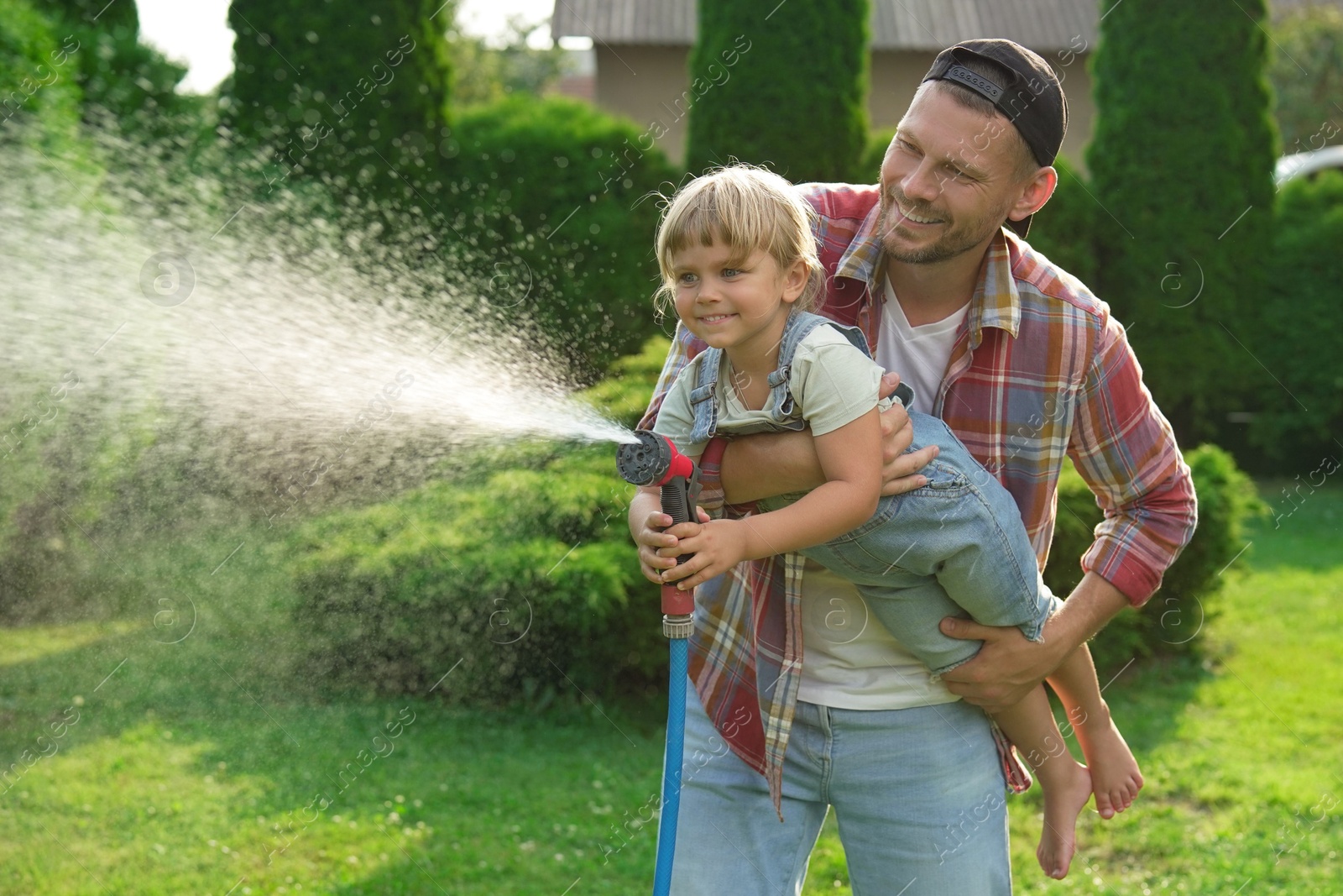 Photo of Father and his daughter watering lawn with hose in backyard