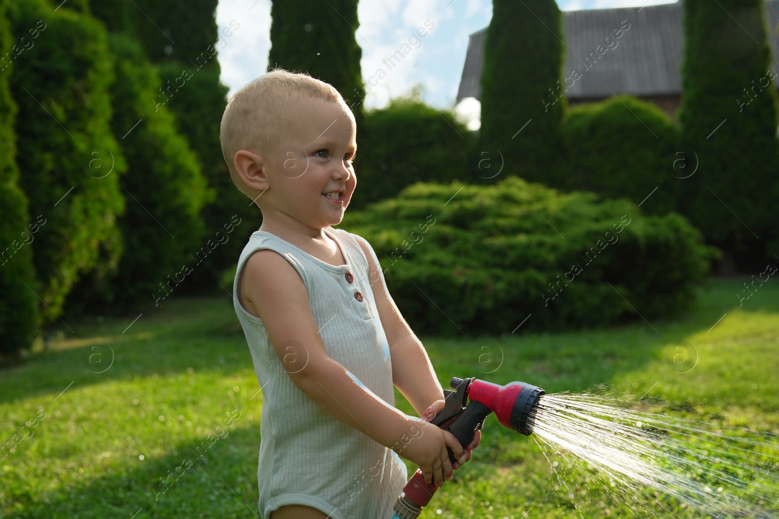 Photo of Little boy watering lawn with hose in backyard