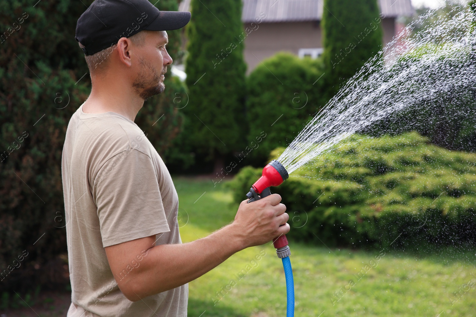 Photo of Man watering lawn with hose in backyard