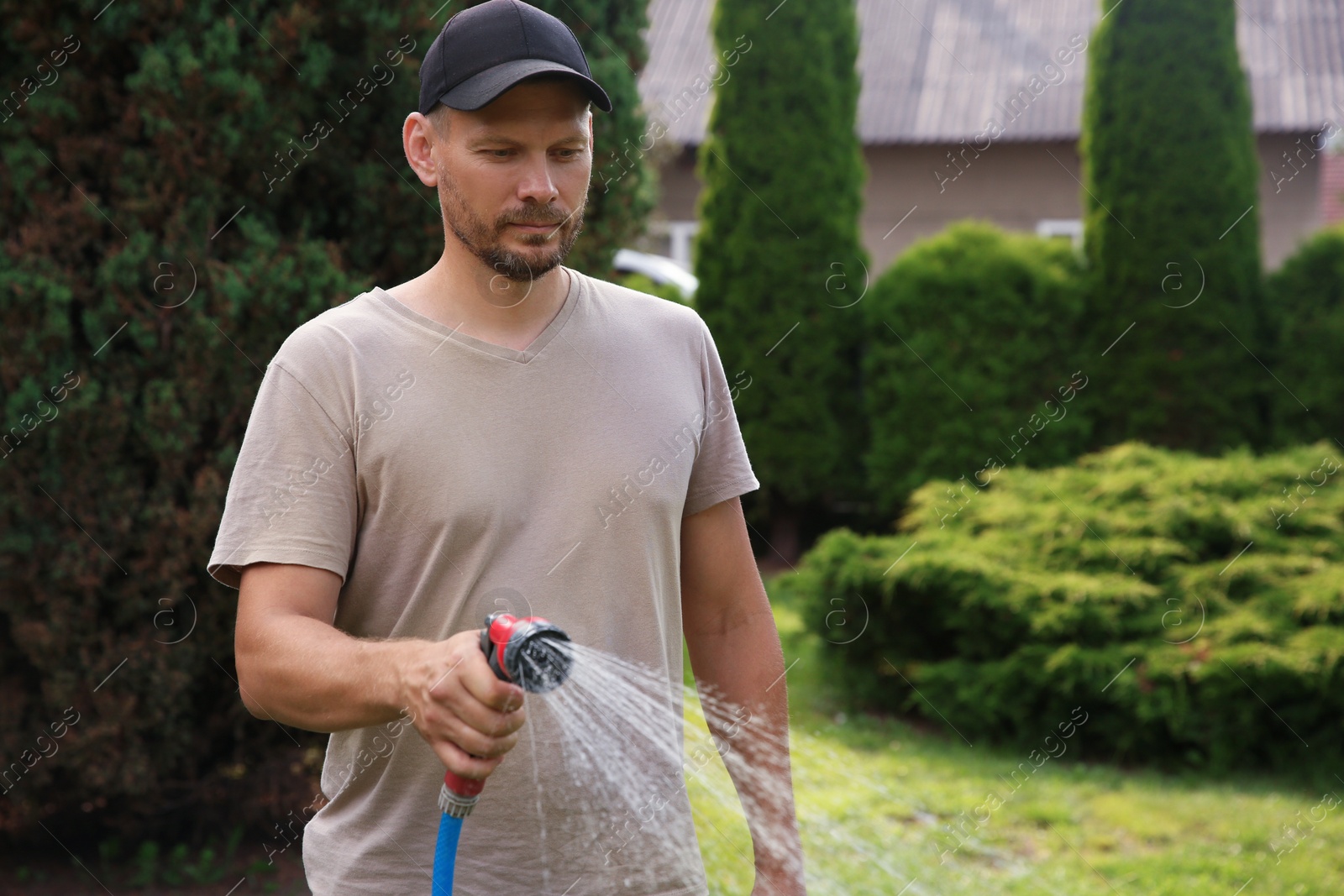 Photo of Man watering lawn with hose in backyard