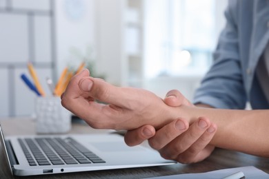 Photo of Man suffering from pain in wrist while working on laptop at table indoors, closeup. Carpal tunnel syndrome