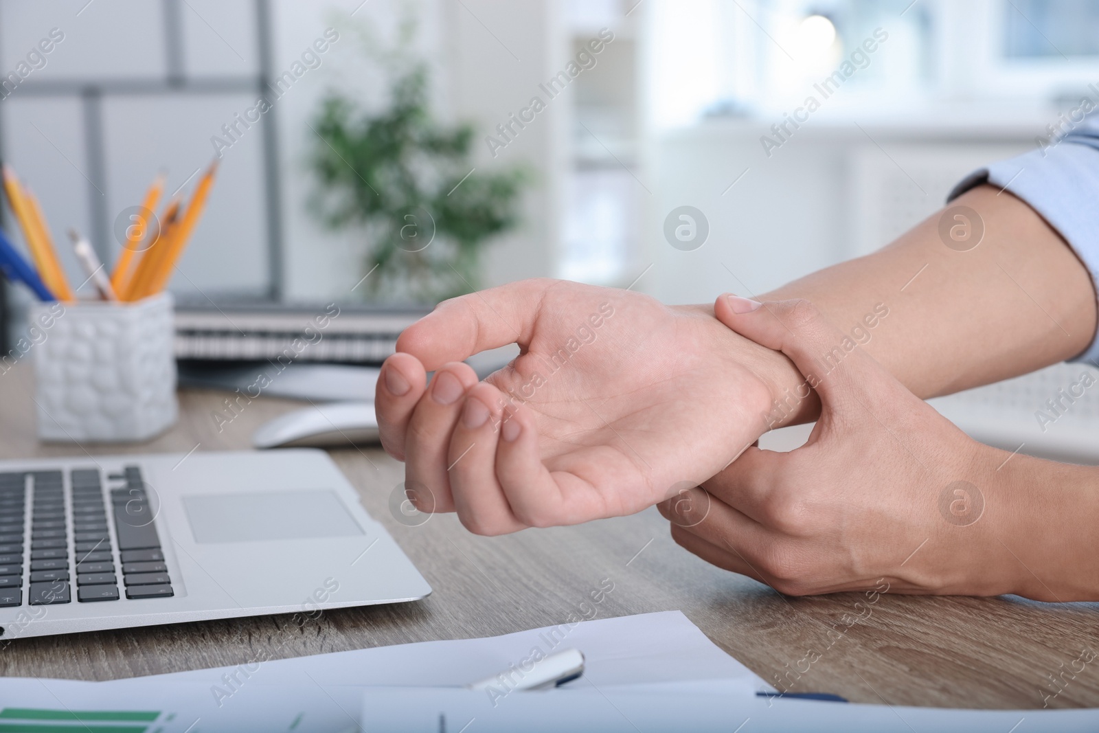 Photo of Man suffering from pain in wrist while working on laptop at table indoors, closeup. Carpal tunnel syndrome