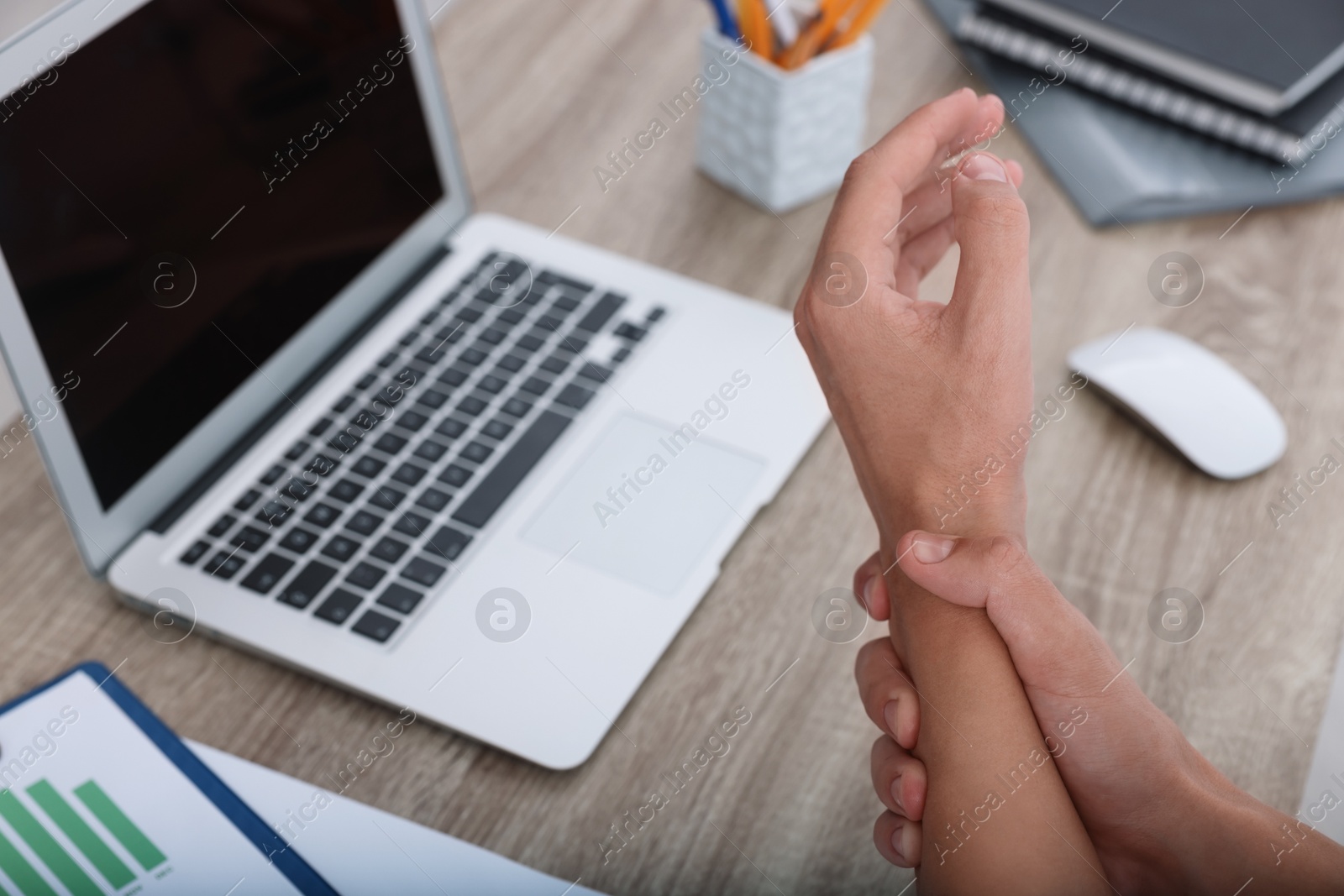 Photo of Man suffering from pain in wrist while working on laptop at table indoors, closeup. Carpal tunnel syndrome