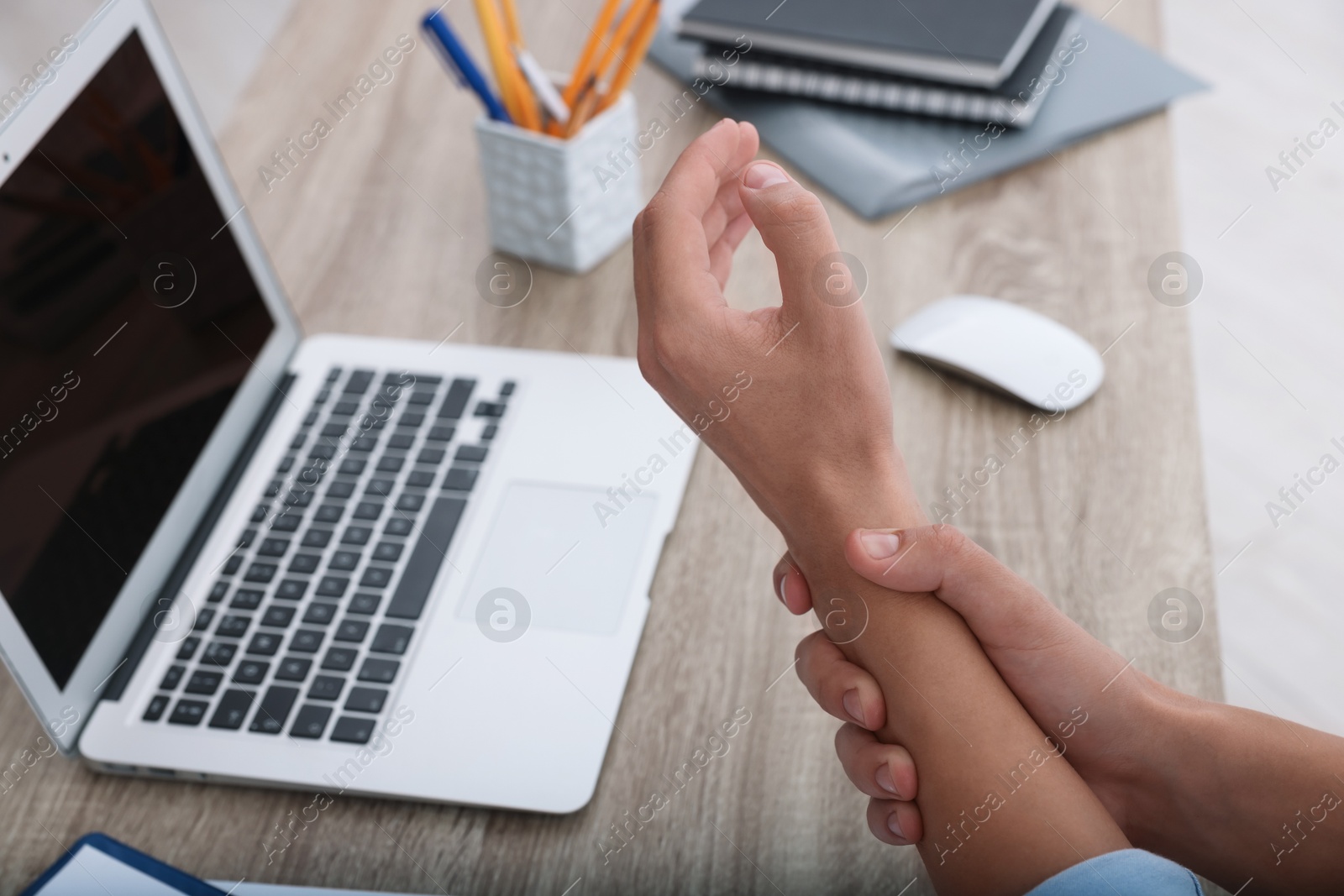 Photo of Man suffering from pain in wrist while working on laptop at table indoors, closeup. Carpal tunnel syndrome