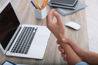 Photo of Man suffering from pain in wrist while working on laptop at table indoors, closeup. Carpal tunnel syndrome