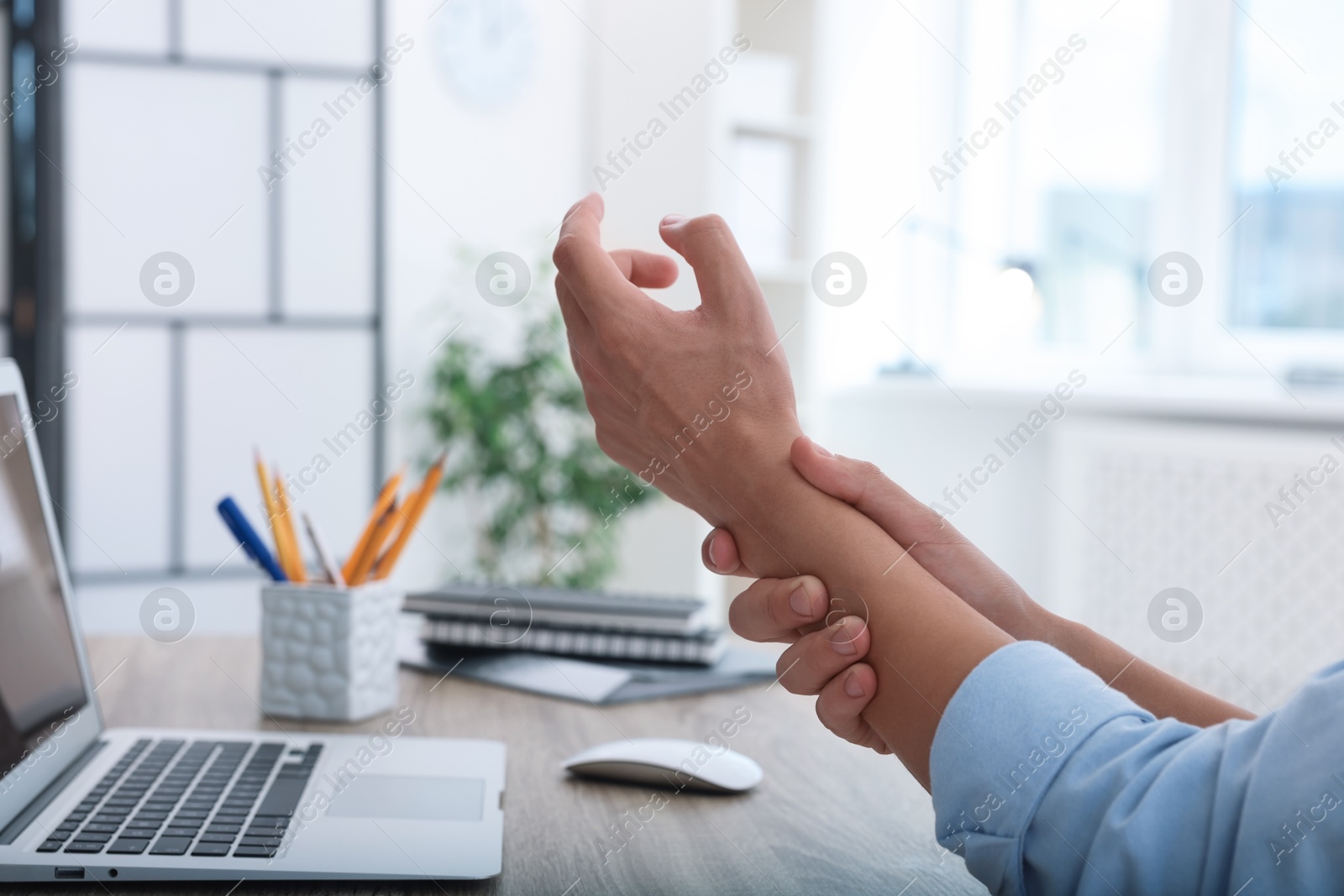 Photo of Man suffering from pain in wrist while working on laptop at table indoors, closeup. Carpal tunnel syndrome