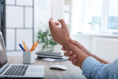 Photo of Man suffering from pain in wrist while working on laptop at table indoors, closeup. Carpal tunnel syndrome