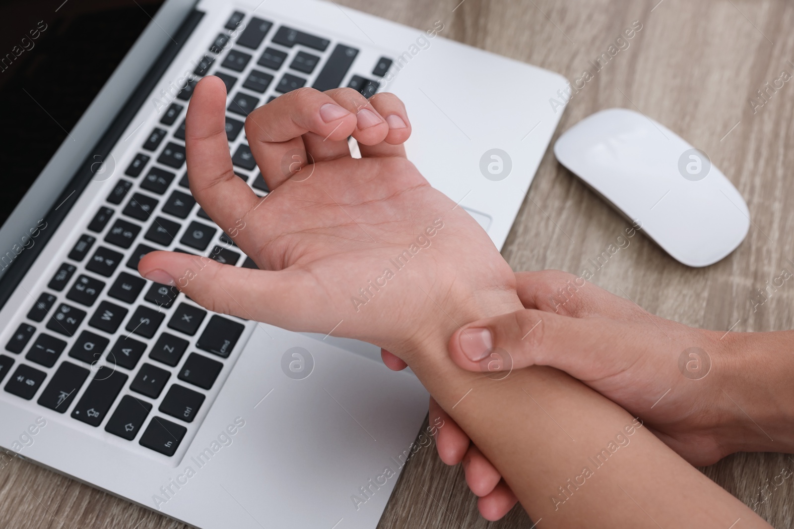 Photo of Man suffering from pain in wrist while working on laptop at wooden table, closeup. Carpal tunnel syndrome