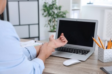 Photo of Man suffering from pain in wrist while working on laptop at table indoors, closeup. Carpal tunnel syndrome