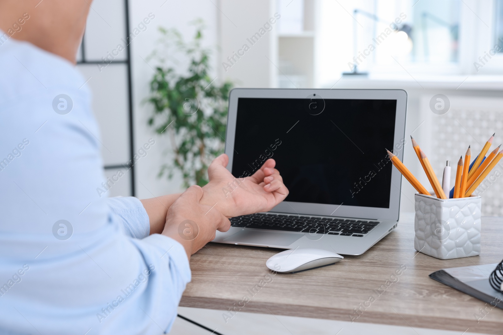 Photo of Man suffering from pain in wrist while working on laptop at table indoors, closeup. Carpal tunnel syndrome