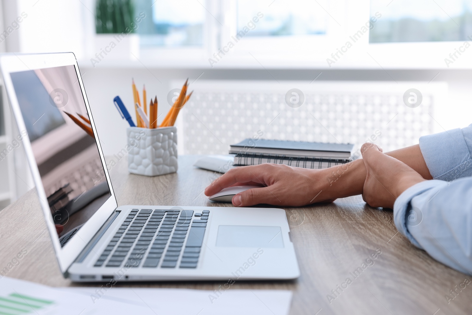 Photo of Man suffering from pain in wrist while using computer mouse at table indoors, closeup. Carpal tunnel syndrome