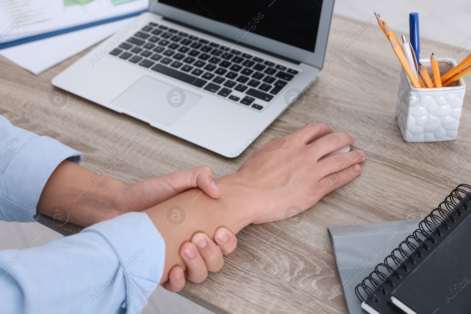 Photo of Man suffering from pain in wrist while using computer mouse at wooden table, closeup. Carpal tunnel syndrome