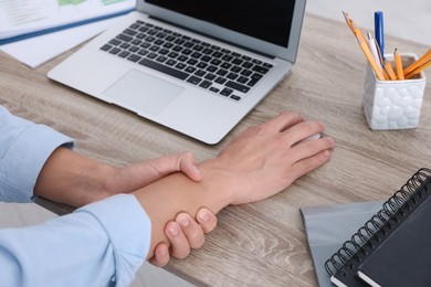 Photo of Man suffering from pain in wrist while using computer mouse at wooden table, closeup. Carpal tunnel syndrome