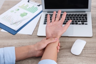 Photo of Man suffering from pain in wrist while working on laptop at wooden table, closeup. Carpal tunnel syndrome