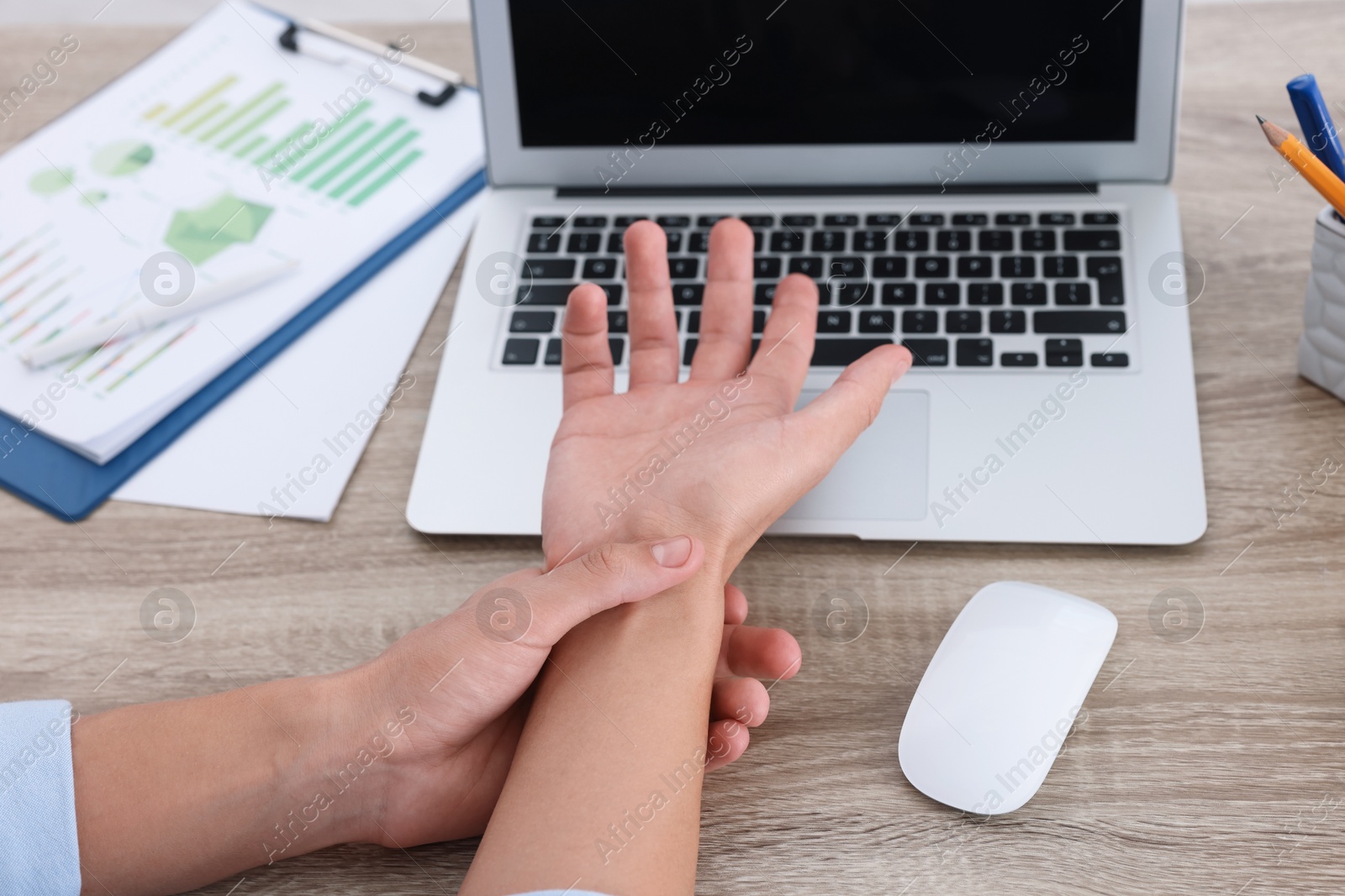 Photo of Man suffering from pain in wrist while working on laptop at wooden table, closeup. Carpal tunnel syndrome