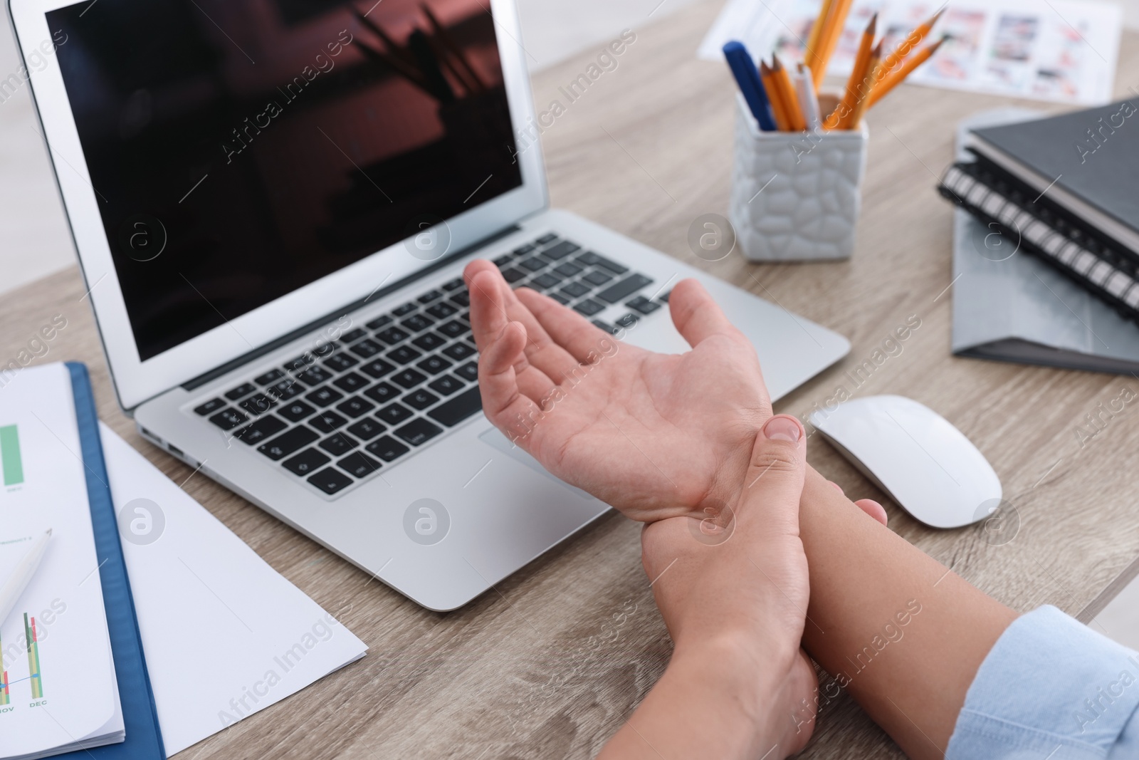 Photo of Man suffering from pain in wrist while working on laptop at table indoors, closeup. Carpal tunnel syndrome