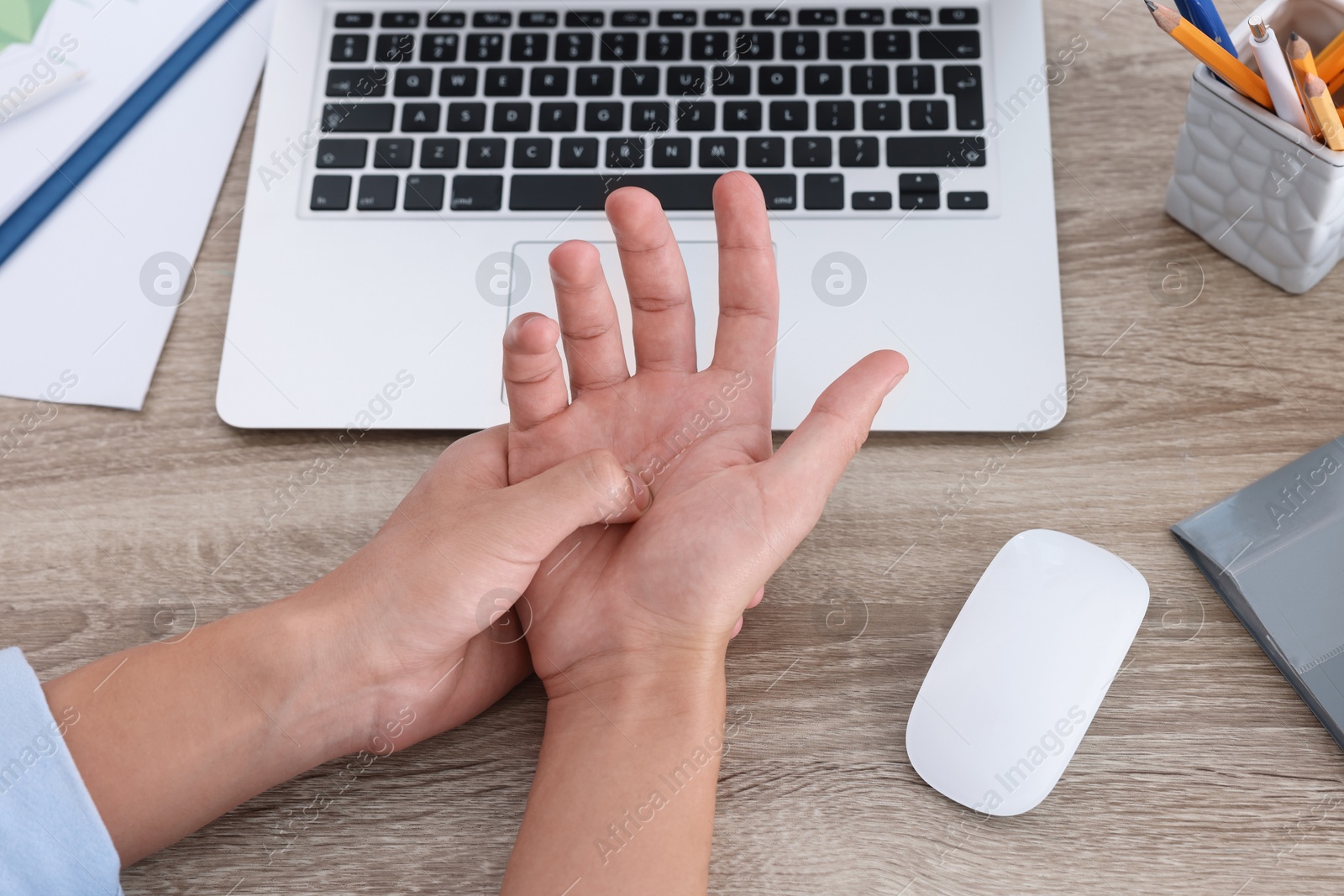 Photo of Man suffering from pain in wrist while working on laptop at wooden table, closeup. Carpal tunnel syndrome