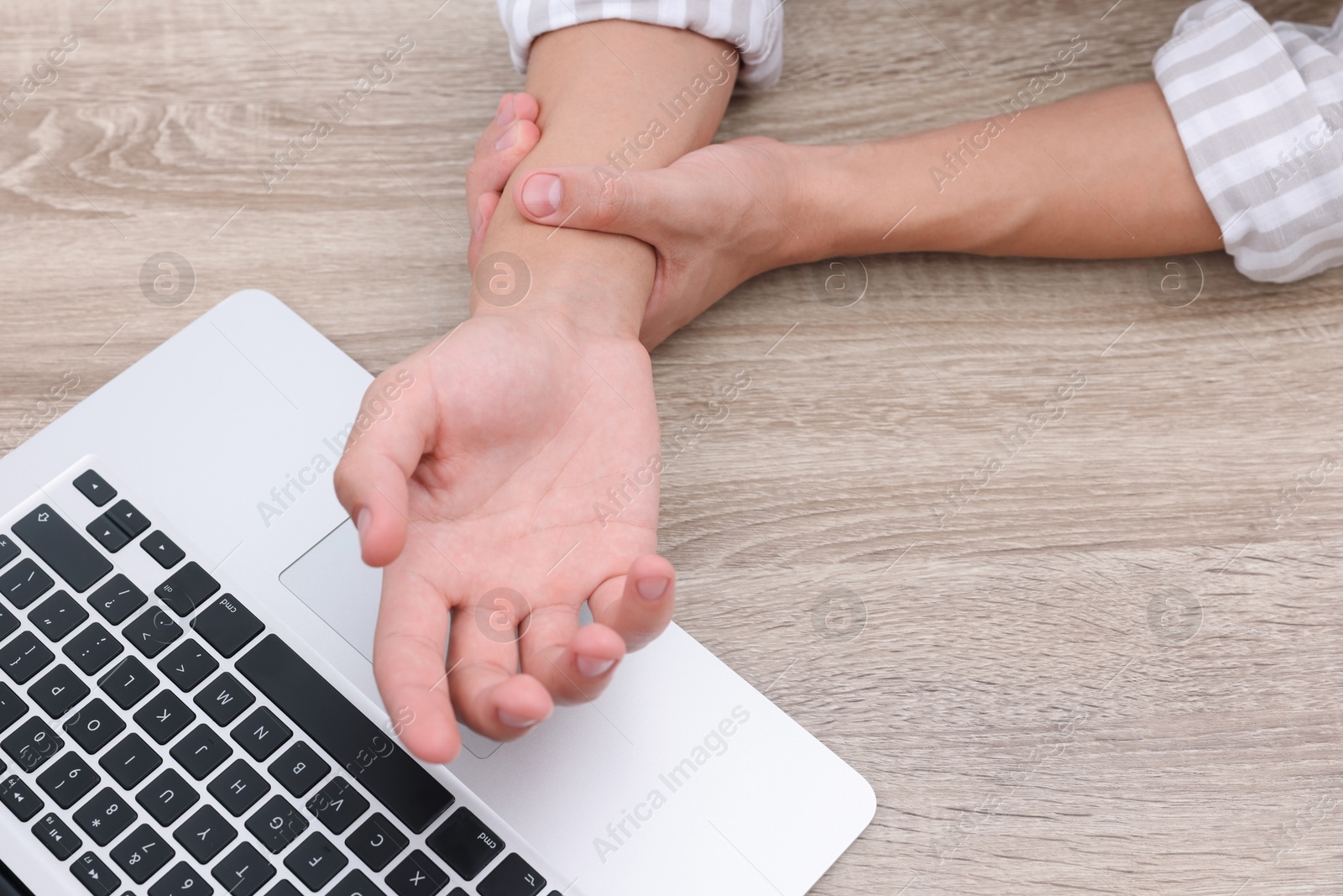 Photo of Man suffering from pain in wrist while working on laptop at wooden table, closeup. Carpal tunnel syndrome