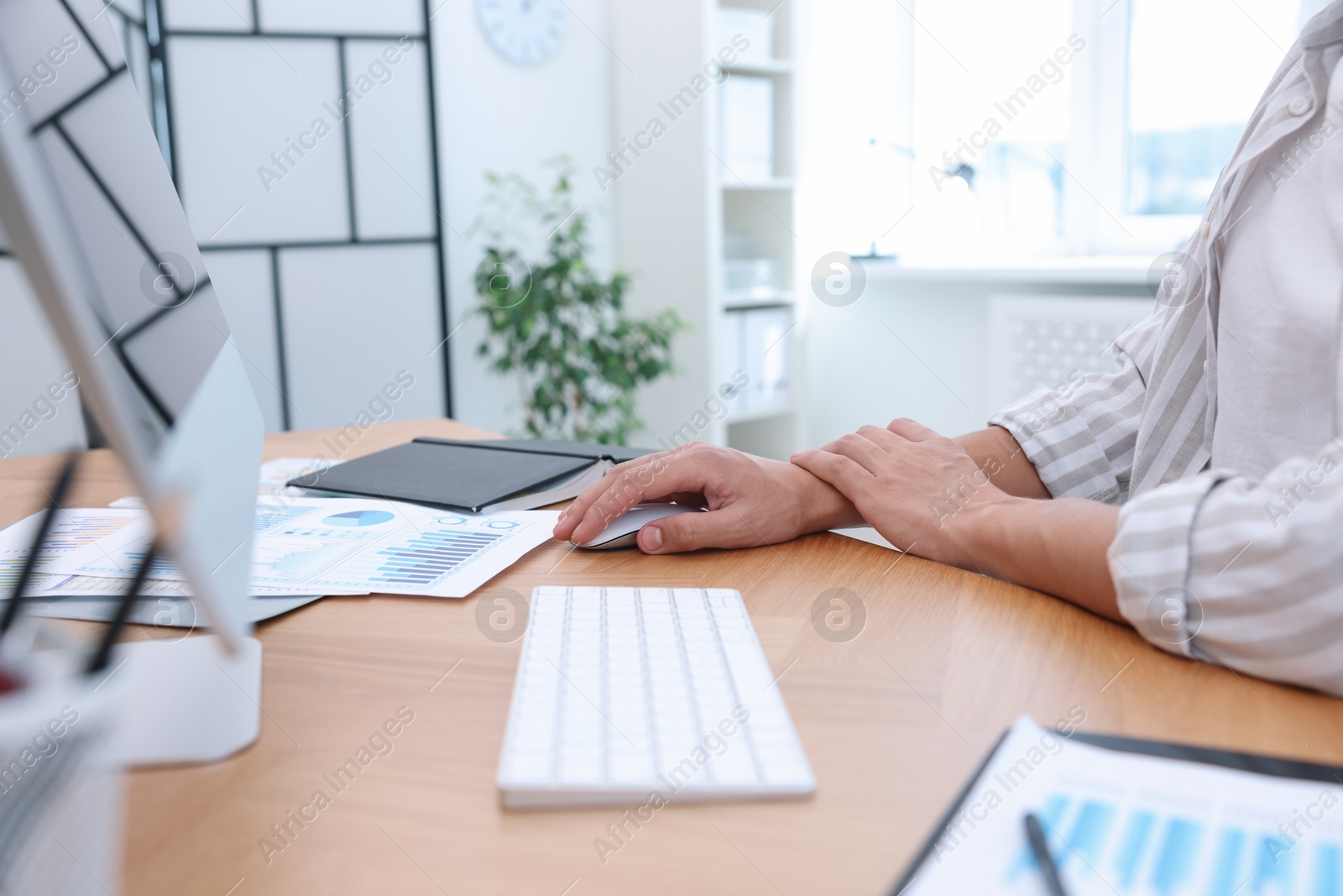 Photo of Man suffering from pain in wrist while using computer mouse at table indoors, closeup. Carpal tunnel syndrome