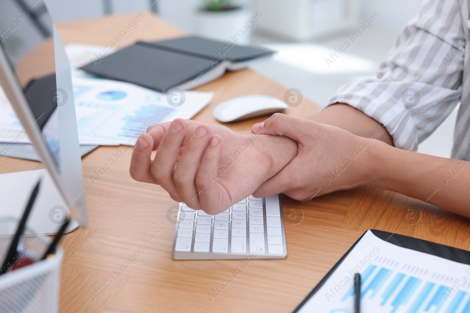 Photo of Man suffering from pain in wrist while working on laptop at table indoors, closeup. Carpal tunnel syndrome