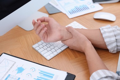 Photo of Man suffering from pain in wrist while working on laptop at table indoors, closeup. Carpal tunnel syndrome