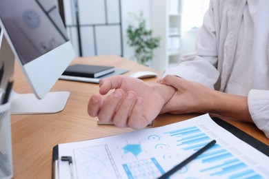 Photo of Man suffering from pain in wrist while working on computer at table indoors, closeup. Carpal tunnel syndrome