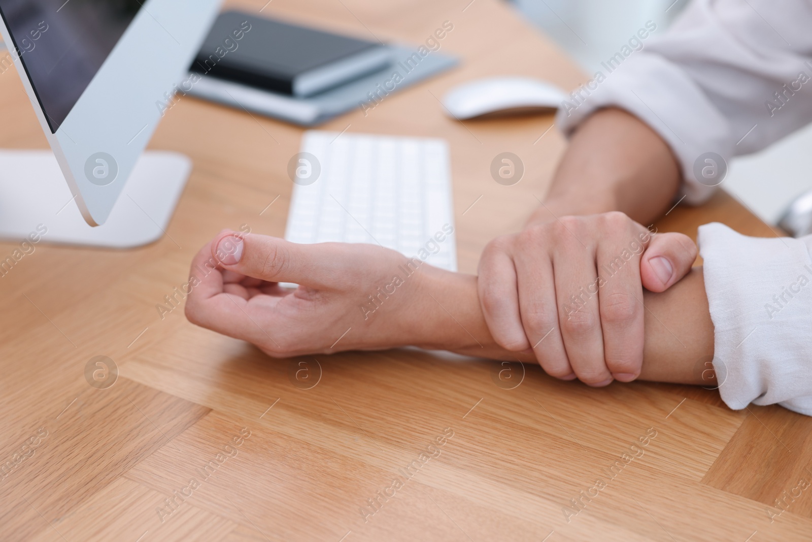 Photo of Man suffering from pain in wrist while working on computer at table indoors, closeup. Carpal tunnel syndrome