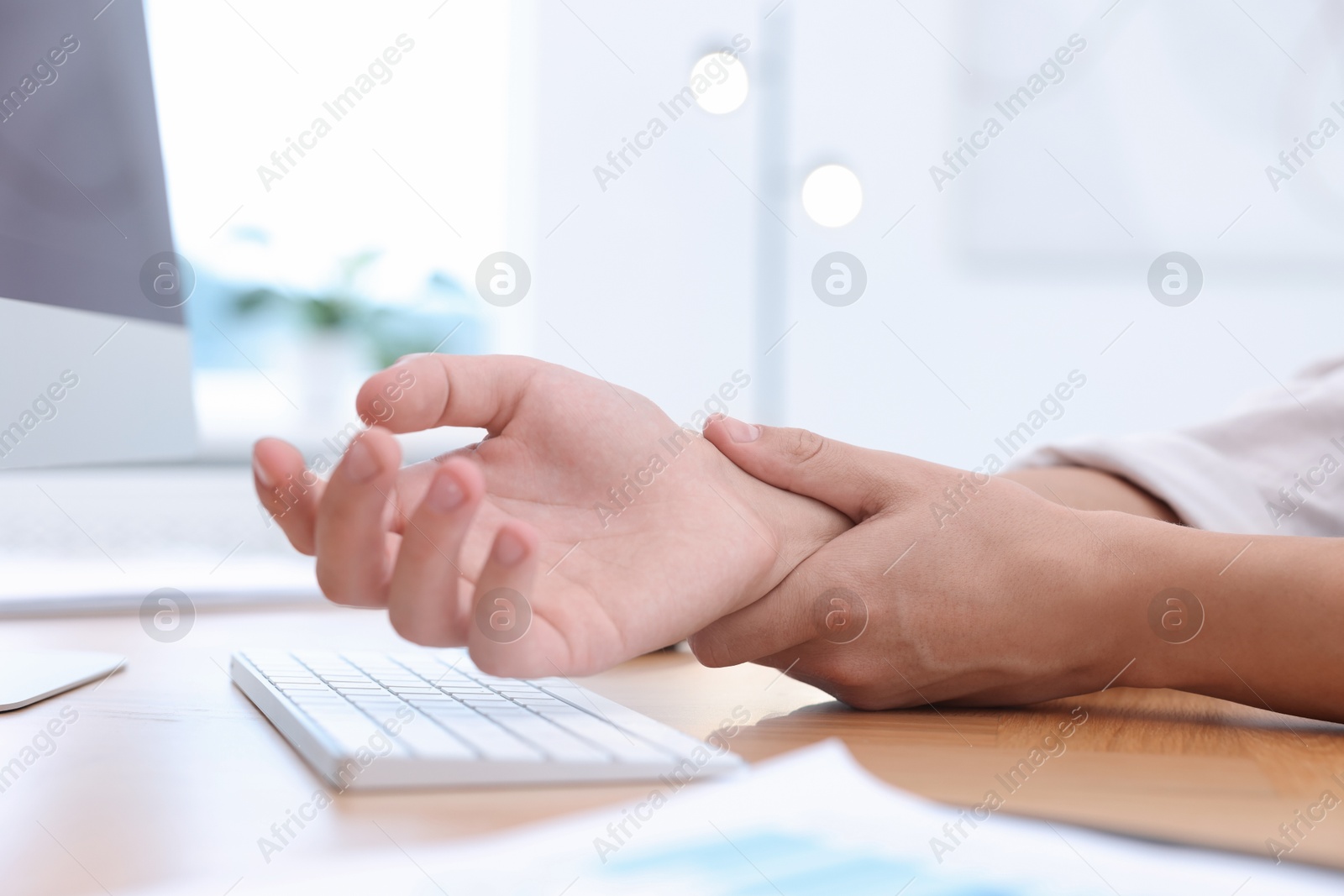 Photo of Man suffering from pain in wrist while working on computer at table indoors, closeup. Carpal tunnel syndrome