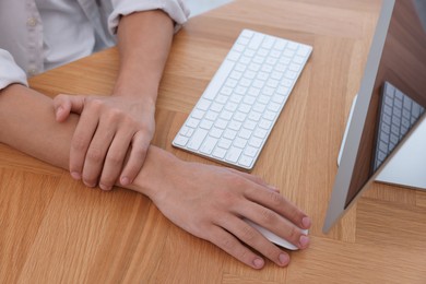 Photo of Man suffering from pain in wrist while working on computer at table indoors, closeup. Carpal tunnel syndrome