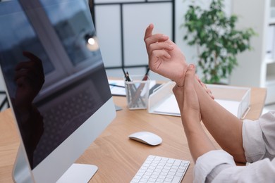 Photo of Man suffering from pain in wrist while working on computer at table indoors, closeup. Carpal tunnel syndrome