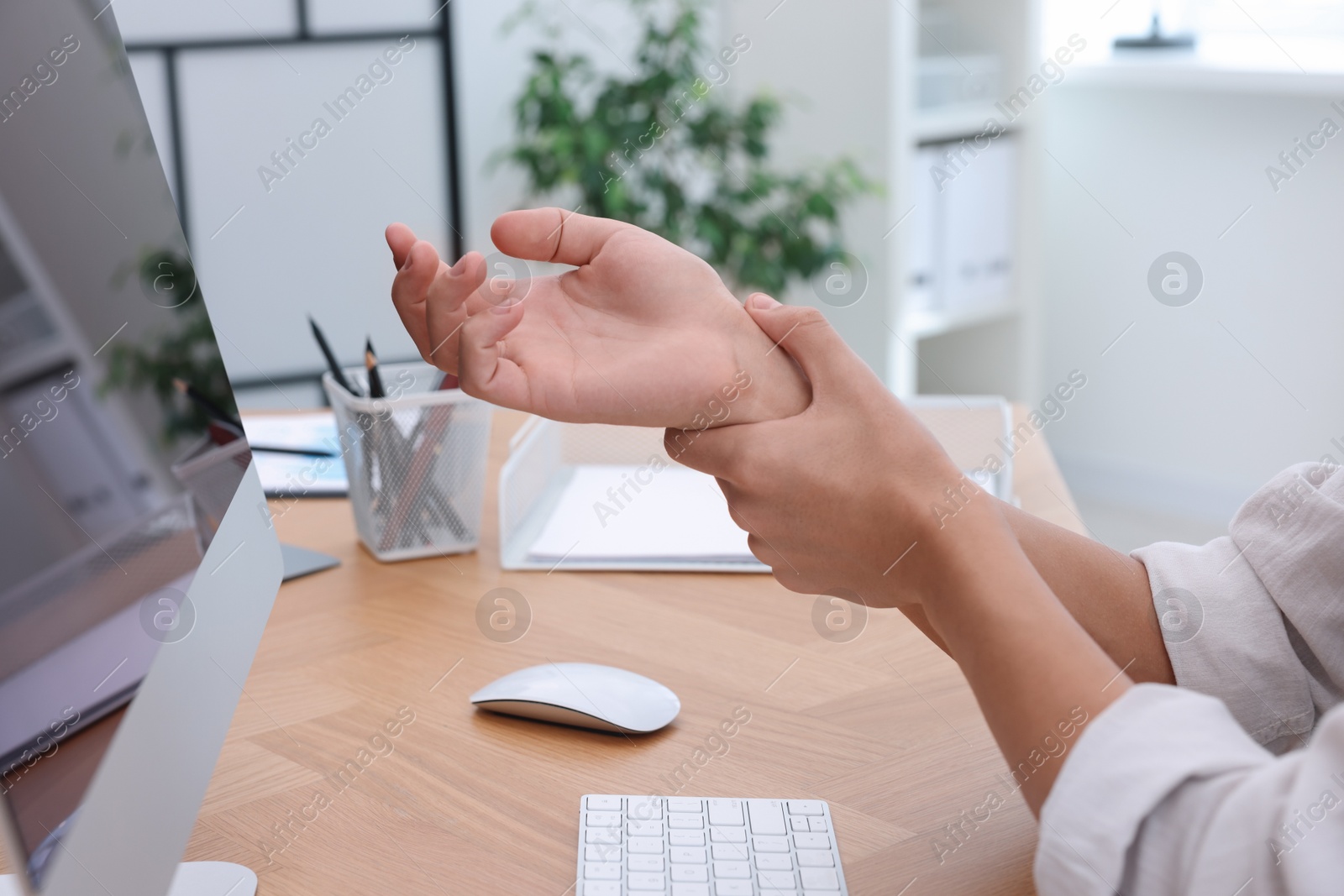 Photo of Man suffering from pain in wrist while working on computer at table indoors, closeup. Carpal tunnel syndrome