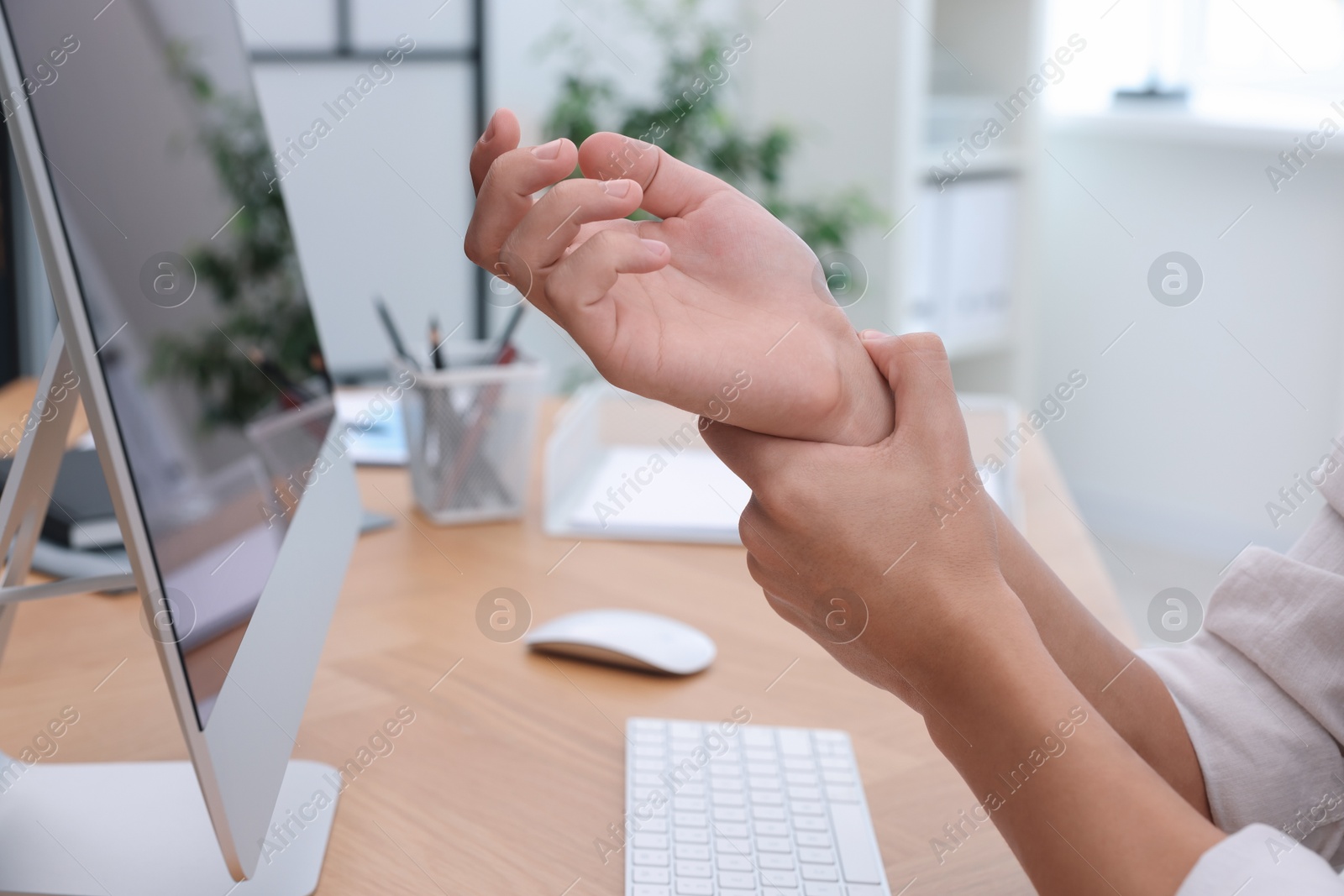 Photo of Man suffering from pain in wrist while working on computer at table indoors, closeup. Carpal tunnel syndrome