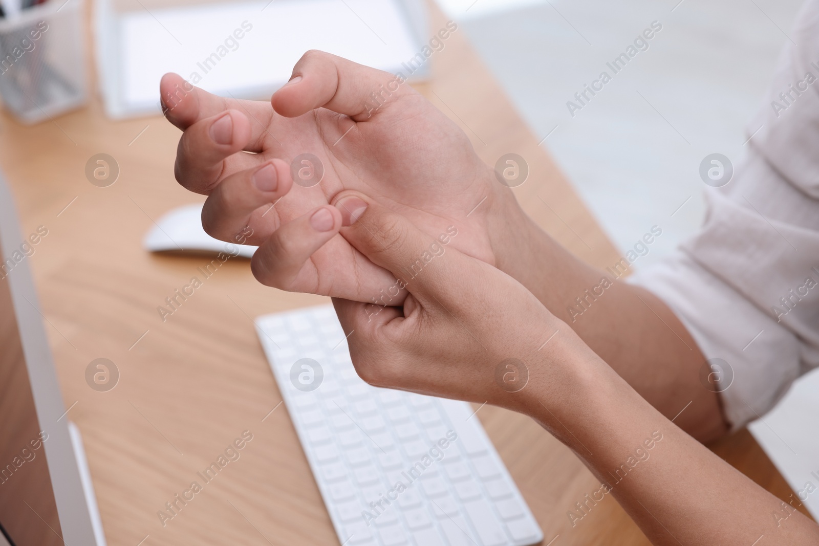 Photo of Man suffering from pain in wrist while working on computer at table indoors, closeup. Carpal tunnel syndrome