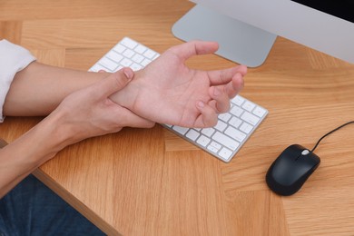 Photo of Man suffering from pain in wrist while working on computer at table indoors, closeup. Carpal tunnel syndrome