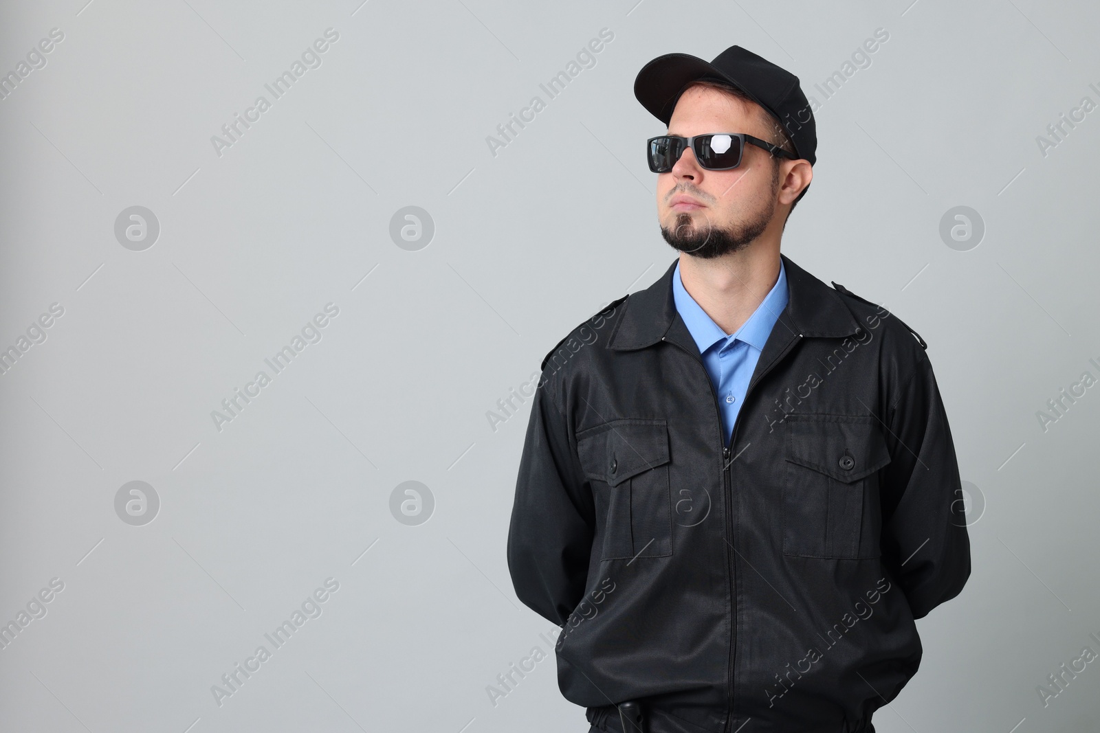 Photo of Security guard in uniform and sunglasses on grey background, space for text