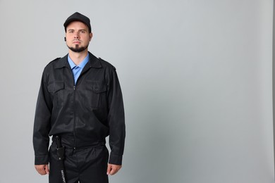 Security guard in uniform with earpiece on grey background, space for text