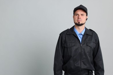 Security guard in uniform with earpiece on grey background, space for text