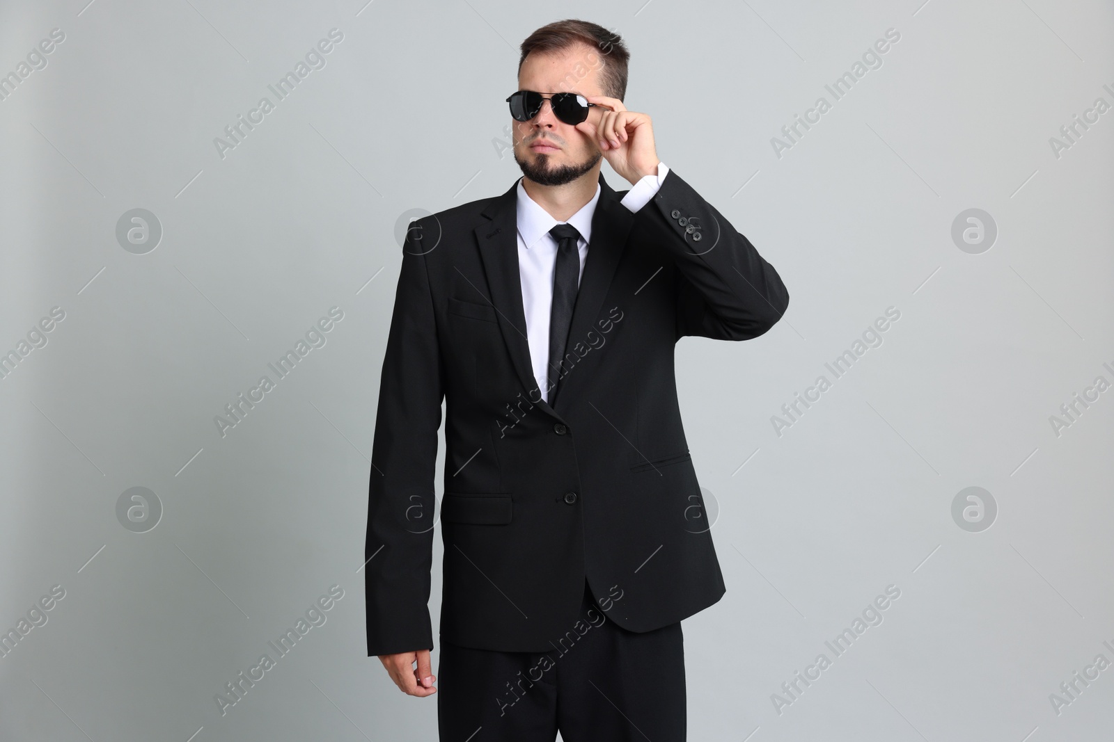 Photo of Young bodyguard in suit and sunglasses on grey background