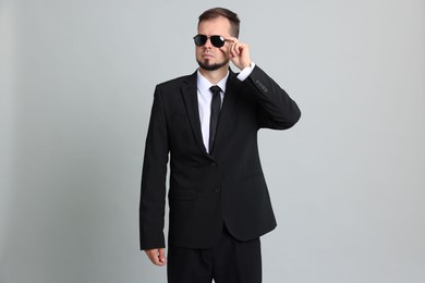 Young bodyguard in suit and sunglasses on grey background