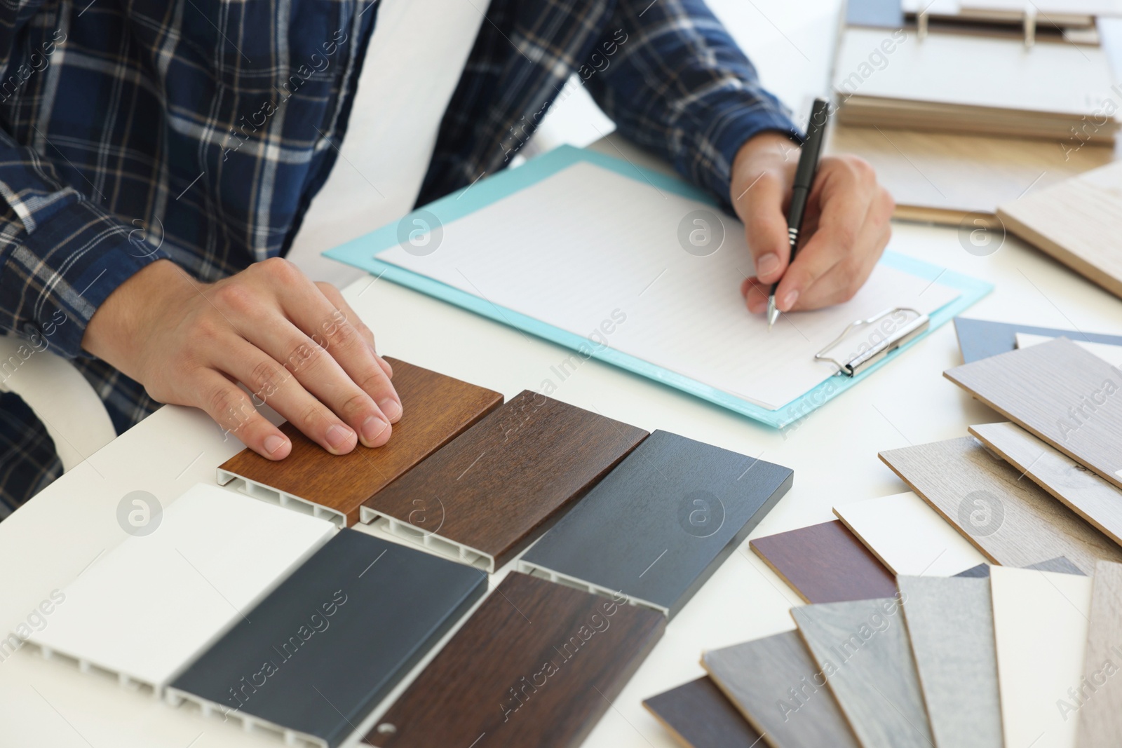 Photo of Man taking notes at table with different samples of wooden flooring indoors, closeup