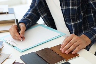 Photo of Man taking notes at table with different samples of wooden flooring indoors, closeup