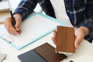 Photo of Man taking notes at table with different samples of wooden flooring indoors, closeup