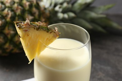 Photo of Tasty pineapple smoothie in glass and fresh fruit on table, closeup