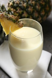 Photo of Tasty pineapple smoothie in glass and fresh fruit on table, closeup