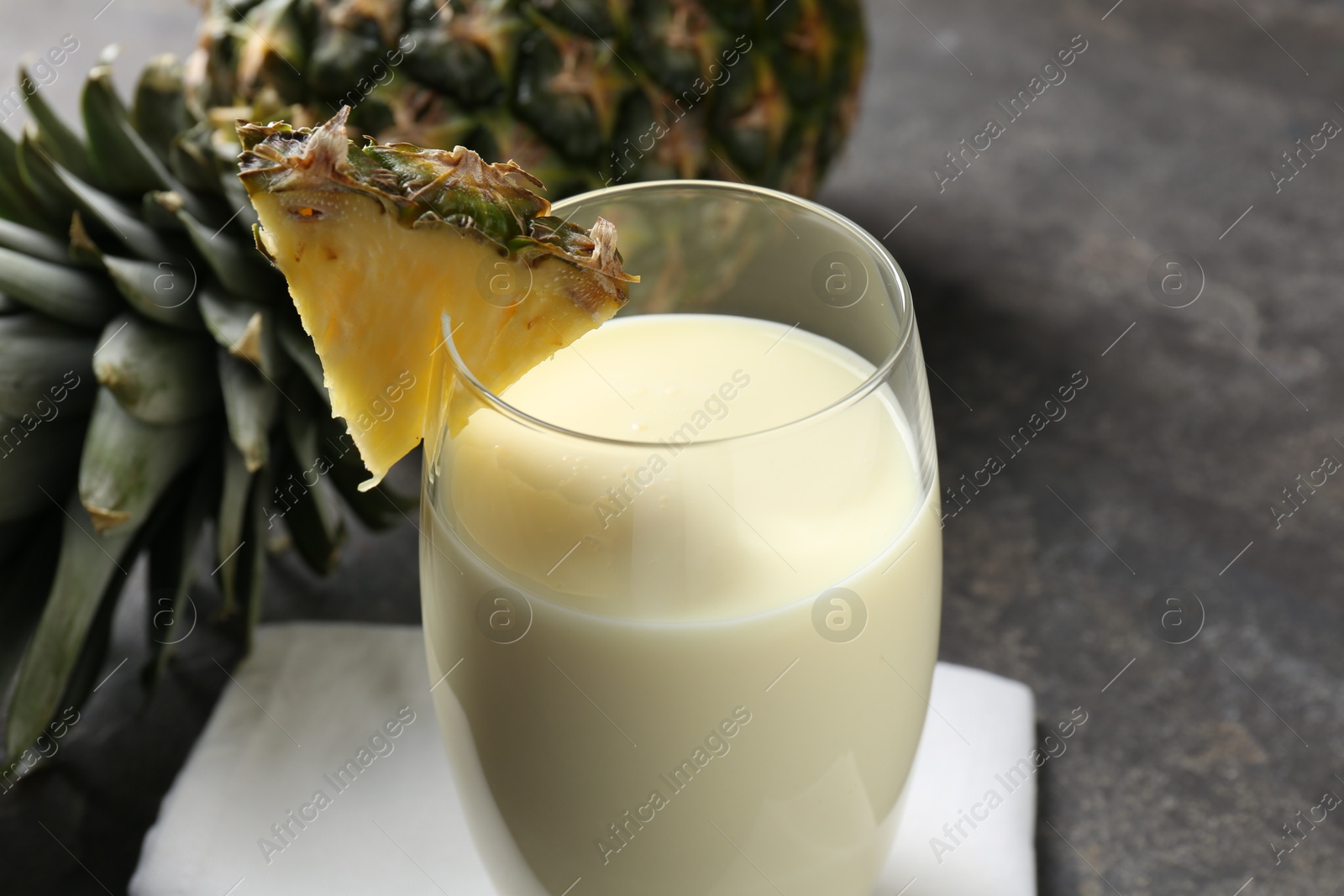 Photo of Tasty pineapple smoothie in glass and fresh fruit on grey table, closeup